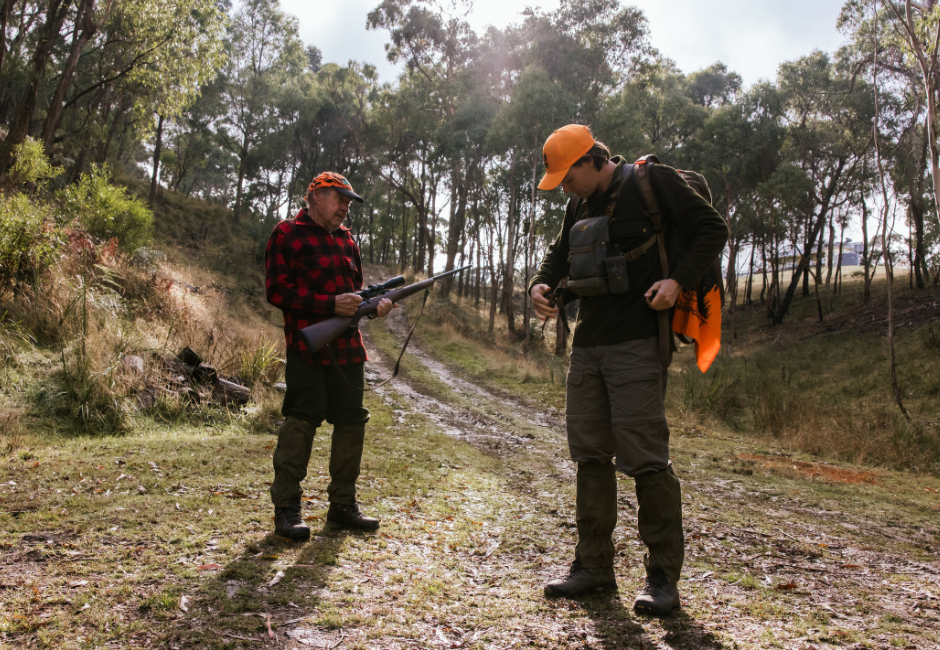 Two hunters. One carries a rifle, the other is checking equipment.